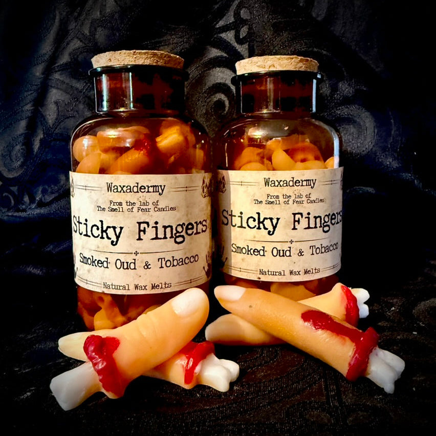 Two bottles labeled 'Sticky Fingers' with wax-like contents on a dark background, accompanied by fake fingers.