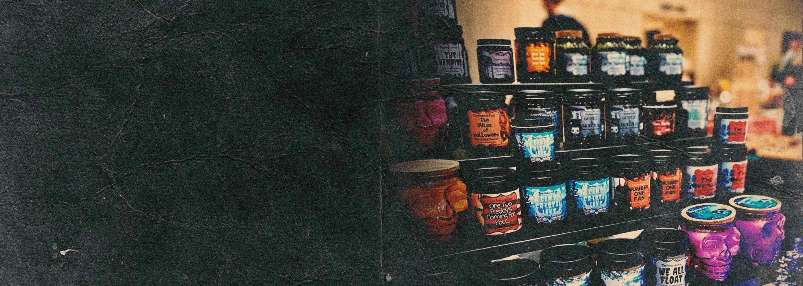 Assorted horror-themed candles in jars and skull containers on display, spooky decor vibe