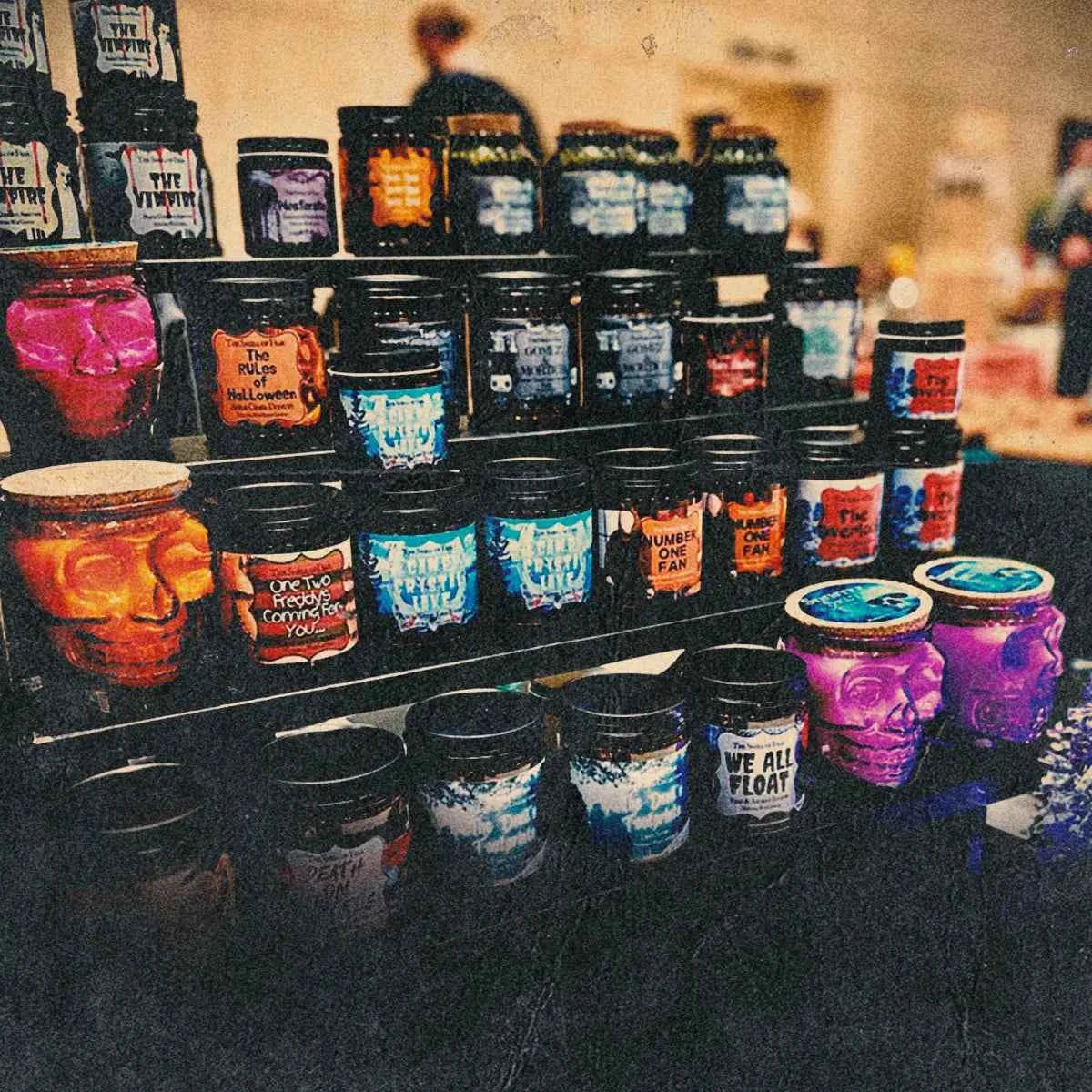 Display of horror-themed candles in skull jars and black tins at a spooky scents market stall
