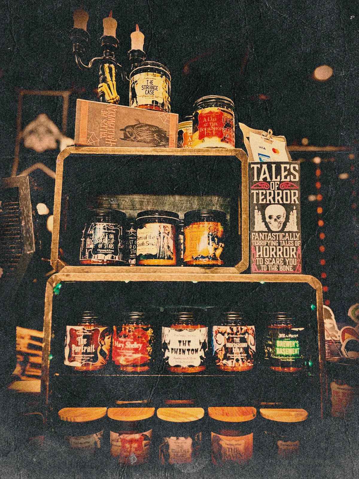 Display of horror-themed candles with gothic labels, spooky decor, and vintage lighting.
