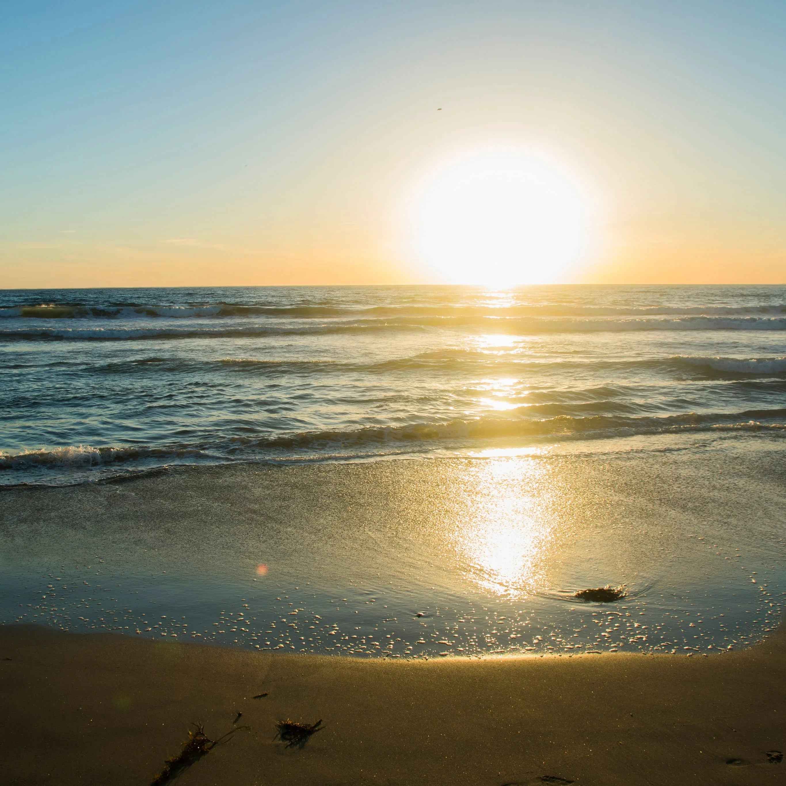 Sunset on a sandy beach with ocean waves and golden sun reflections on the water